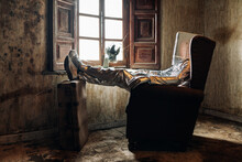 Side View Unrecognizable Person Wearing Protective Silver Suit With Box On Head Resting On Armchair In Shabby Room In Abandoned House