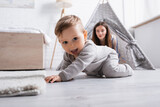 Fototapeta  - excited baby boy crawling on floor near mother on blurred background