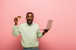 © LIGHTFIELD STUDIOS - amazed african american man showing credit card while holding laptop on pink background