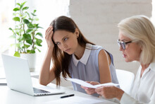 Unhappy Young Female Employee Bored With Middle-aged Colleague Discuss Paper Document At Meeting. Tired Woman Worker Bothered Annoyed By Senior Coworker Lecture About Paperwork At Team Briefing.