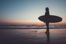 Silhouette Of Beautiful Sexy Surfer Female With Surfboard On The Sandy Beach At Sunset. Water Sports. Surfing Are Healthy Active Lifestyle. Summertime Vacation.