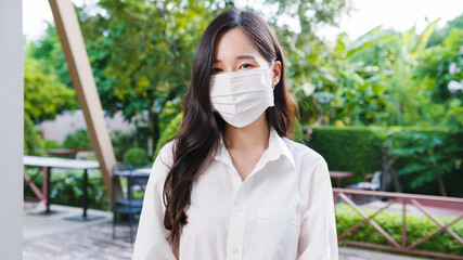 Young Asia businesswoman wear protective face mask looking at camera outside during Covid-19 coronavirus health crisis in street in city. Lifestyle new normal after corona virus and social distancing.