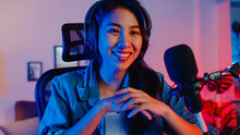 Happy Asia Girl Blogger Music Influencer Looking At Camera Broadcast Record Wear Headphone Online Live Talk In Microphone With Audience In Living Room Home Studio At Night. Content Creator Concept.