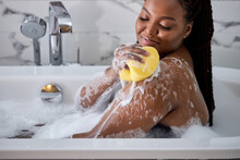 African Woman Washing Herself, Taking Bath With Sponge At Home, Free Space. Side View On Delighted Relaxed Lady Taking Care About Body, Wellness Concept