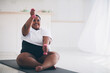 happy young plus size woman exercising with weights on sport mat at home, muscules warm-ups