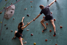 Two Athletes Climber Moving Up On Steep Rock, Climbing On Artificial Wall Indoors Together Supporting And Helping, In Sportive Outfit. Extreme Sports And Bouldering Concept