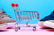 New sneakers toes and small shopping cart on a pink and blue background. Close up. Shopping concept