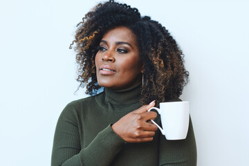 Wall Mural - Closeup studio portrait of calm African American Black thoughtful Woman with curly hair Enjoying Coffee looking at the window