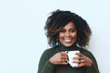 Wall Mural - Closeup studio portrait of smiling African American Black Woman with curly hair holding white cup drinking coffee