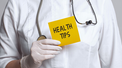 Wall Mural - Cropped view of doctor in a white coat and sterile gloves holding a note with words - Health Tips