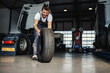 © Dusan Petkovic - Smiling hardworking mechanic rolling tire in order to change it on truck. He is in garage of import and export firm.