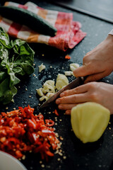 Wall Mural - Vertical shot of hands cutting peppers on the black surface in the kitchen