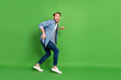 Full length body size photo of thief sneaking away looking back scared afraid stole something isolated vibrant green color background