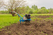 A blue walk-behind tractor stands on arable land. Agricultural vehicles cultivate the land. Arable land, vegetable garden.