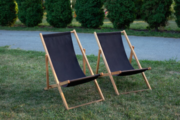 Deckchairs in autumn garden. Two deckchairs on summer green lawn. Lounge sunbed. Wooden garden furniture on grass lawn outdoor for relax. Backyard exterior. Garden landscape with chairs in nature.