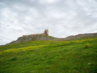 Canvas Print - Enisala fortress ruins in a green field under a cloudy sky in the Dobrogea region, Romania