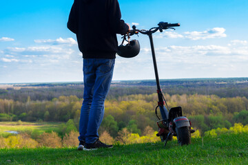 Wall Mural - A young man on an electric scooter , modern transport. Enjoy nature from a hill on the observation deck . Spring and summer time