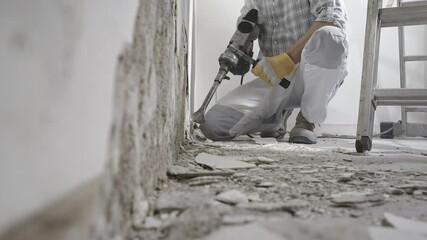 Wall Mural - House renovation concept. Construction worker with protective gloves at work breaks the wall with the jackhammer, plaster rubble and ladder on the white background.