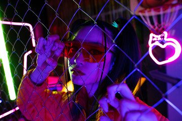 trendy young asian woman in sunglasses looking at camera through metallic fence