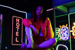 brunette young asian woman sitting near neon sign with hotel lettering outside