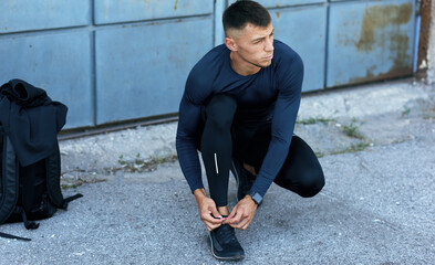 Jogger male tying shoelaces during running outdoors. The man pulls the laces for his shoes on the concrete pavement.