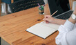© NAMPIX - woman hand writing on notebook with pencil while sitting at the table in modern office.