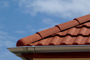 half round ridge tiles and shallow zink gutter in grey silver color. textured modern concrete tile roof. closeup detail. house construction concept. light blue sky background