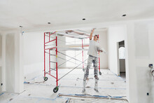 Tradesman On Stilts Plastering Drywall In Home