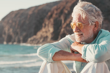 Wall Mural - Beautiful bearded senior man sitting on the beach looking at horizon and sunset light