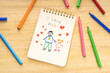 © Formatoriginal - Fathers day concept. Notebook with drawing of a father with a girl and marker pens on a wooden table