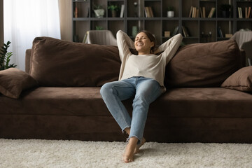 Pleasure of being alone. Peaceful teenage female recline on cozy sofa in modern flat relax with closed eyes enjoy tranquility. Happy young lady rest on couch at tidy living room after cleaning is done