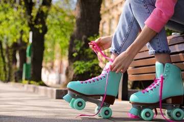 Poster - Woman lacing roller skates while sitting on bench outdoors, closeup