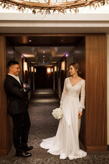 Wall Mural - Romantic meeting of the bride and groom in the hotel corridor. The groom gives the bride a wedding bouquet of white roses. Morning before the wedding.