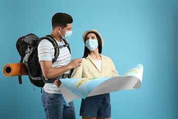 Poster - Couple of tourists in medical masks with map on light blue background. Travelling during coronavirus pandemic