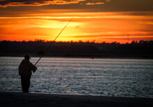 Silhouette Man Fishing In Sea Against Sunset Sky