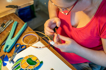 young woman is making a stained glass,  piece of glass is lined in foil along the edges