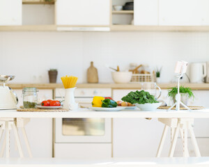 Cooking healthy food. Italian pasta, fresh vegetables, pumpkin seeds, scales and other ingredients on white wooden table against blurred kitchen counter background in modern light apartment