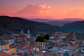 Wall Mural - Aerial view of colorful dense buildings surrounded by mountains under an orange sunset sky