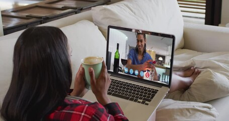 Poster - African american woman holding a coffee cup having a video call on laptop sitting on couch at home