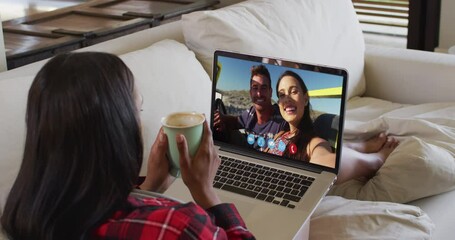 Poster - African american woman holding a coffee cup having a video call on laptop sitting on couch at home