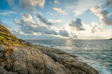 Wall Mural - Rocky ocean coast in front of beautiful sunset lights, waves hits rocks in cloudy weather