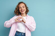© Drobot Dean - Young ginger woman with wavy hair smiling and showing heart gesture