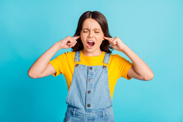 Poster - Photo of annoyed irritated small school girl wear denim jeans overall fingers close ears screaming isolated blue color background