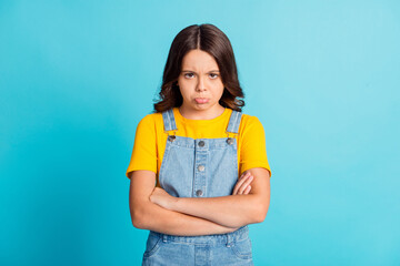 Wall Mural - Photo of funny upset small school girl wear denim jeans overall arms folded isolated blue color background