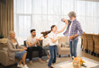 Loving grandfather dancing with cute little girl granddaughter in front of grandmother and parents relaxing on sofa in living room at home. Happy family enjoying leisure time and having fun together
