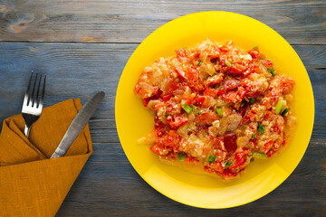 Wall Mural - Stewed tomatoes with onions in a plate on a wooden background