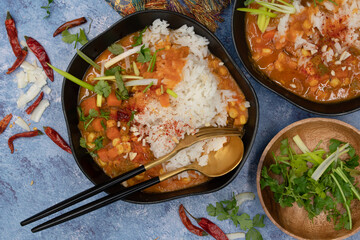 Vegan thai red curry woth rice in stylsih black bowls on textured table