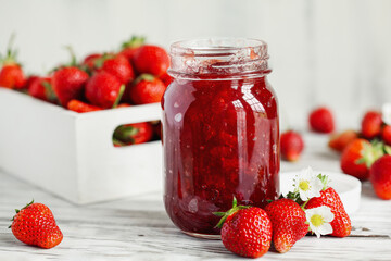 Homemade strawberry preserves or jam in a mason jar surrounded by fresh organic strawberries. Selective focus with blurred foreground and background.