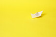 A paper boat on a bright yellow background.