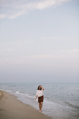 Wall Mural - Carefree hipster woman walking barefoot on sandy beach with sea waves in the evening, enjoying tranquil moment. Casual young female  relaxing on seashore at resort. Mindfulness